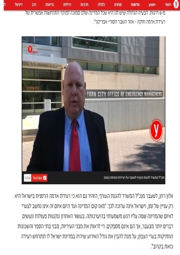A man in a suit stands outside the New York City Office of Emergency Management building, speaking in a video with Hebrew text above and below.